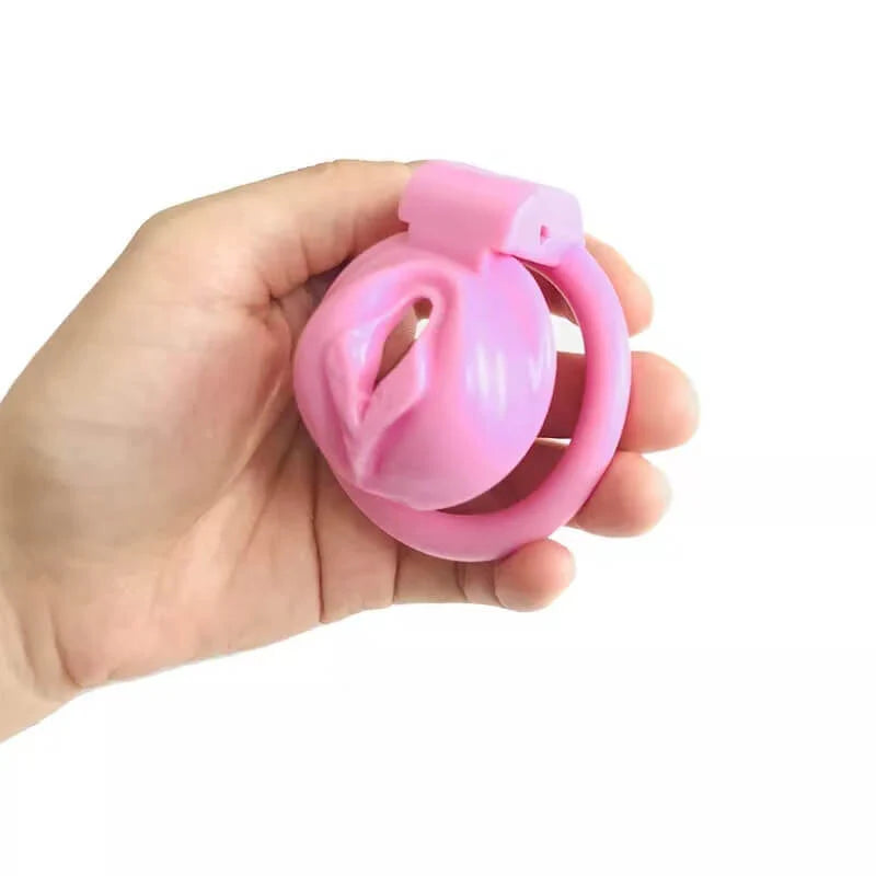 Hand holding a pink pussy-shaped male chastity cage showing side profile on a white background